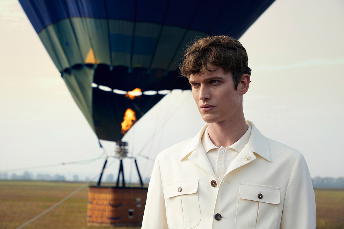 Tombolini campaign: a model in a cream tailored jacket stands in a field in front of a hot air balloon.